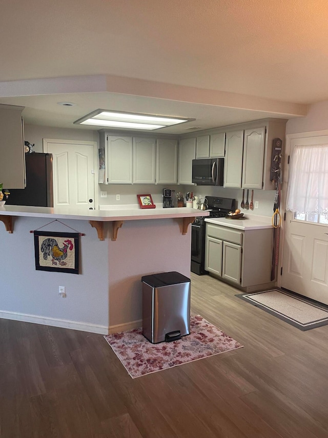 kitchen with a kitchen breakfast bar, black appliances, kitchen peninsula, and light hardwood / wood-style flooring