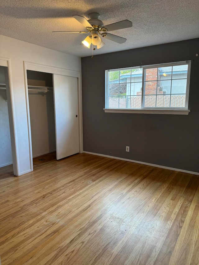 unfurnished bedroom featuring ceiling fan, a textured ceiling, light wood-type flooring, and two closets