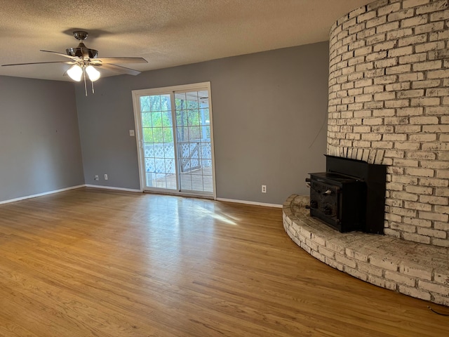 unfurnished living room featuring ceiling fan, a textured ceiling, light wood-type flooring, and a wood stove