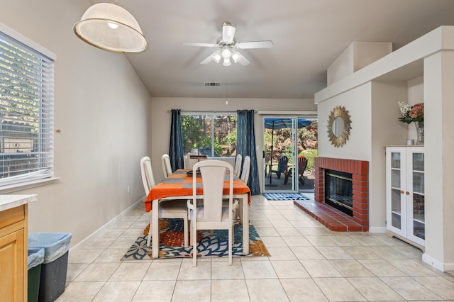 tiled dining space with ceiling fan and a brick fireplace