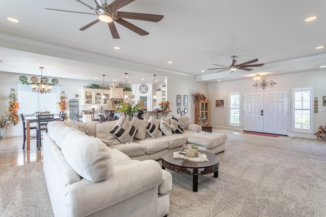 carpeted living room with ceiling fan with notable chandelier and crown molding