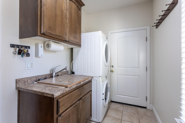 laundry room with sink, cabinets, light tile patterned floors, and stacked washer / dryer