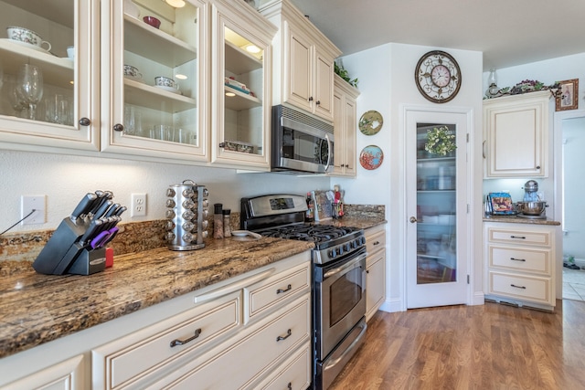 kitchen featuring stone counters, cream cabinetry, light wood-type flooring, and stainless steel appliances