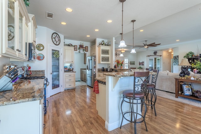 kitchen featuring stainless steel refrigerator, ceiling fan, hanging light fixtures, dark stone countertops, and a kitchen bar