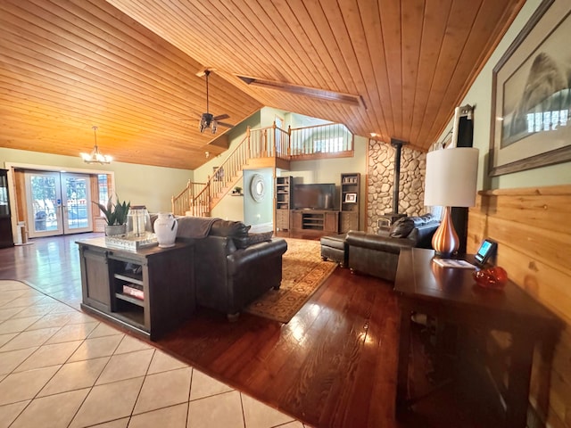 living room featuring ceiling fan with notable chandelier, a wood stove, vaulted ceiling with beams, and wood ceiling