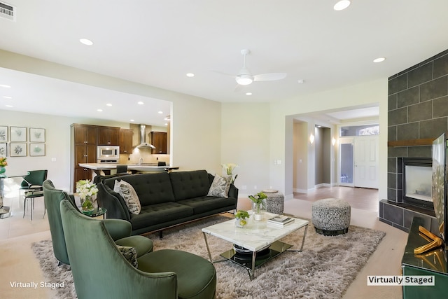 living room featuring light wood-type flooring, a tile fireplace, and ceiling fan