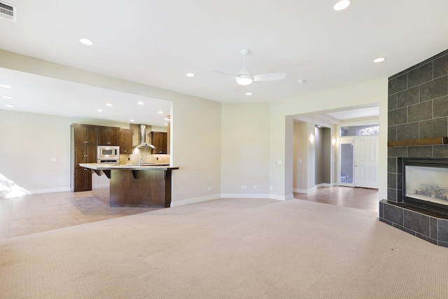 unfurnished living room featuring light carpet, ceiling fan, and a tile fireplace