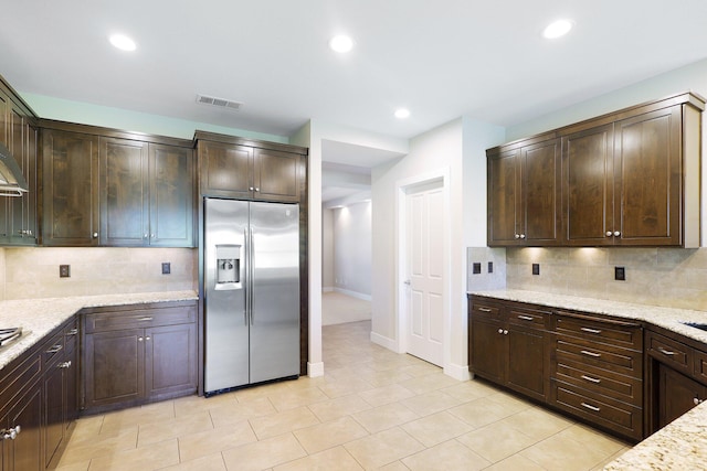 kitchen featuring light stone counters, stainless steel refrigerator with ice dispenser, dark brown cabinets, and tasteful backsplash