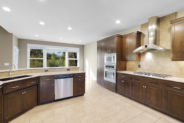 kitchen with dark brown cabinetry, sink, wall chimney exhaust hood, stainless steel appliances, and light stone countertops