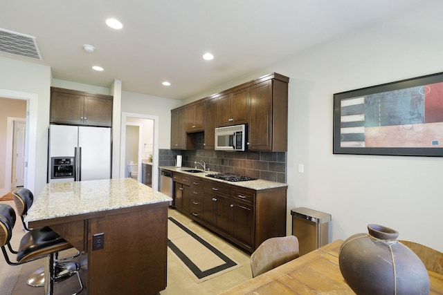 kitchen with a kitchen breakfast bar, decorative backsplash, stainless steel appliances, a center island, and sink