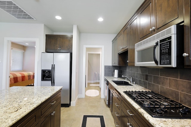 kitchen featuring light stone countertops, appliances with stainless steel finishes, dark brown cabinetry, and sink