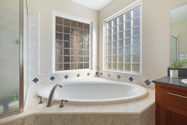 bathroom featuring vanity, a relaxing tiled tub, and plenty of natural light