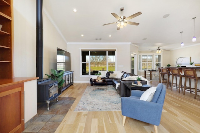 living room featuring ceiling fan, a wood stove, and ornamental molding