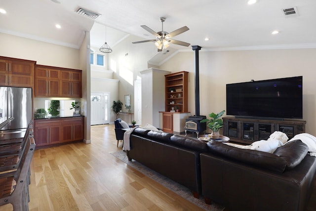 living room with ceiling fan with notable chandelier, light wood-type flooring, a wood stove, and crown molding