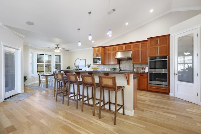 kitchen featuring a kitchen bar, backsplash, ceiling fan, a center island with sink, and hanging light fixtures