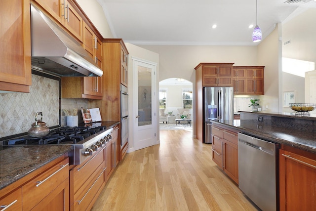 kitchen featuring light wood-type flooring, tasteful backsplash, stainless steel appliances, dark stone countertops, and hanging light fixtures