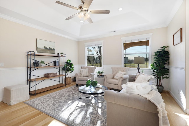 living room featuring ceiling fan, a raised ceiling, crown molding, and light hardwood / wood-style flooring