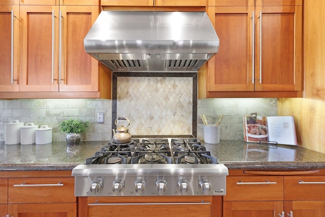 kitchen with dark stone counters, tasteful backsplash, stainless steel gas stovetop, and wall chimney exhaust hood