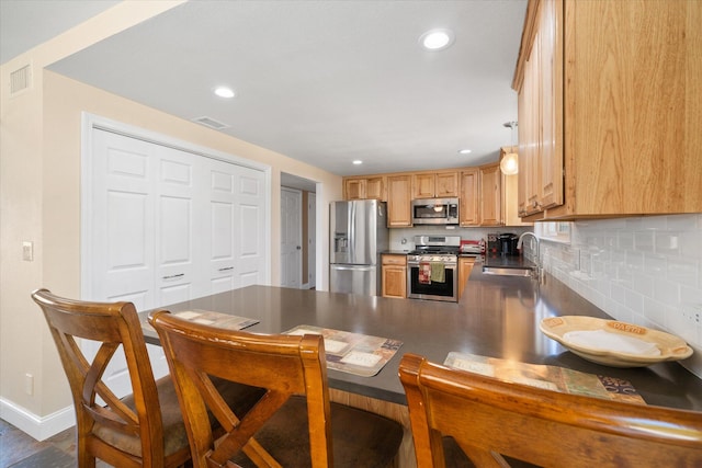 kitchen with sink, kitchen peninsula, backsplash, dark wood-type flooring, and appliances with stainless steel finishes