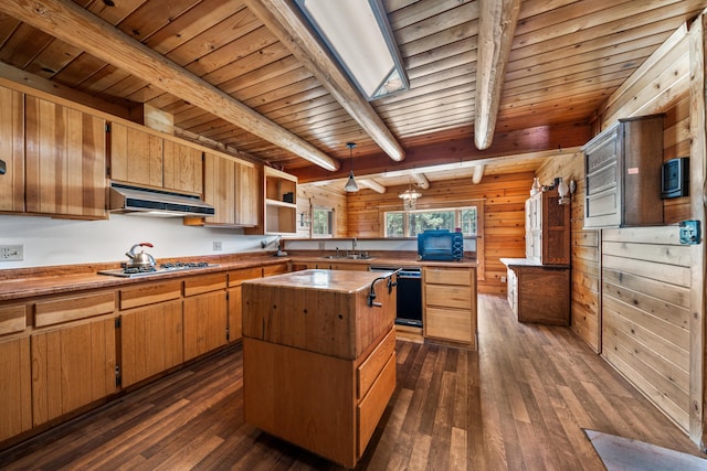 kitchen with hanging light fixtures, dark wood-type flooring, a kitchen island, exhaust hood, and beam ceiling