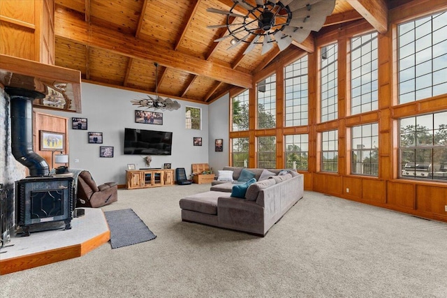 carpeted living room with a wood stove, beam ceiling, high vaulted ceiling, ceiling fan, and wooden ceiling