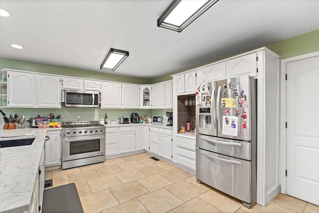 kitchen with stainless steel appliances, white cabinetry, light tile patterned floors, and sink