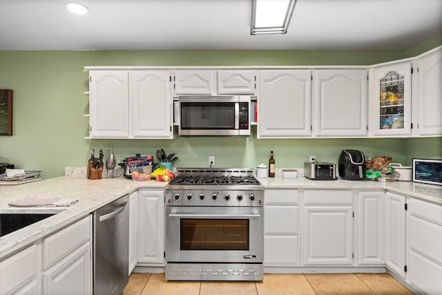 kitchen featuring light stone countertops, white cabinets, appliances with stainless steel finishes, and light tile patterned floors