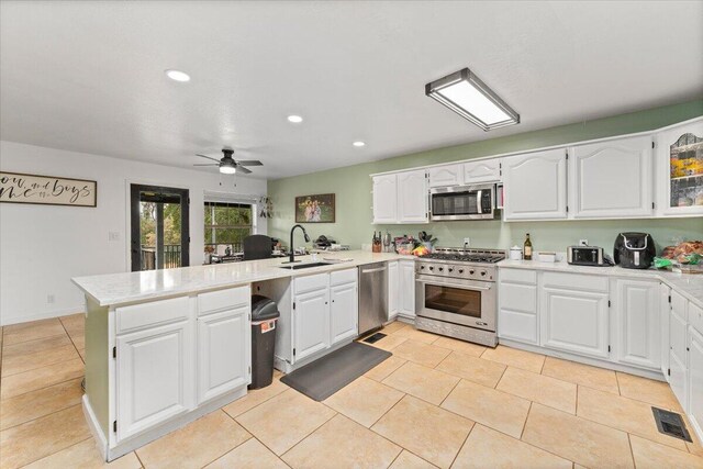 kitchen with appliances with stainless steel finishes, white cabinets, kitchen peninsula, ceiling fan, and sink