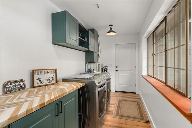 clothes washing area featuring washer and clothes dryer, light hardwood / wood-style flooring, and cabinets