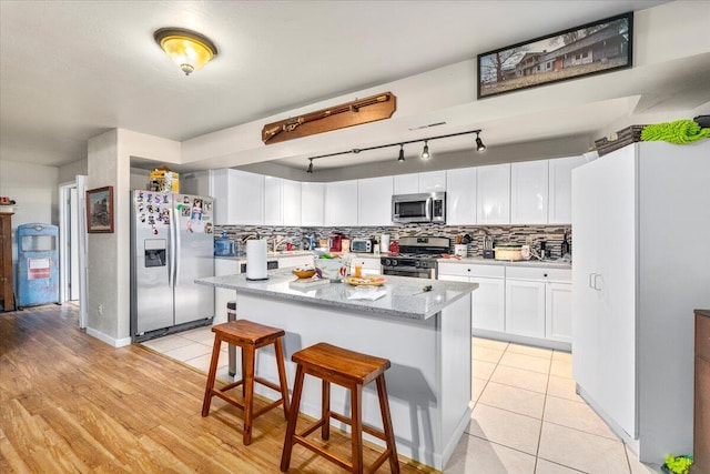 kitchen with a breakfast bar, light stone counters, white cabinets, a kitchen island, and stainless steel appliances