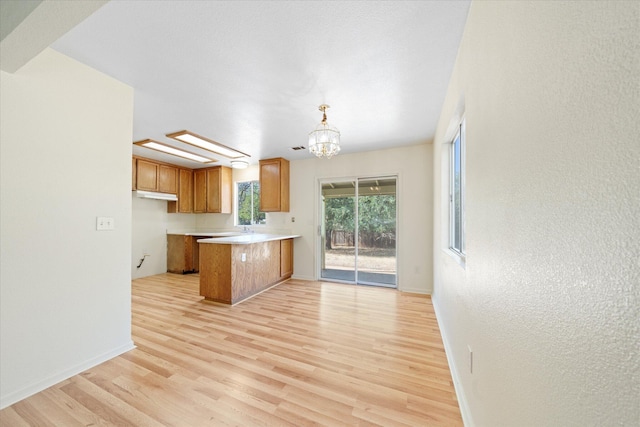 kitchen featuring pendant lighting, kitchen peninsula, light hardwood / wood-style flooring, and an inviting chandelier