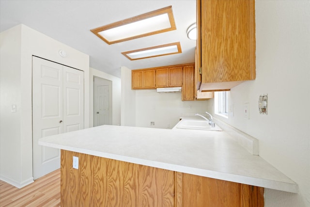 kitchen with light wood-type flooring, kitchen peninsula, and sink