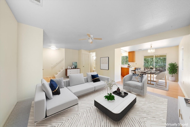 carpeted living room with ceiling fan with notable chandelier