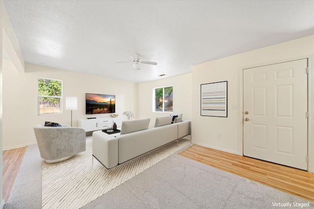 living room with ceiling fan, a textured ceiling, and light wood-type flooring