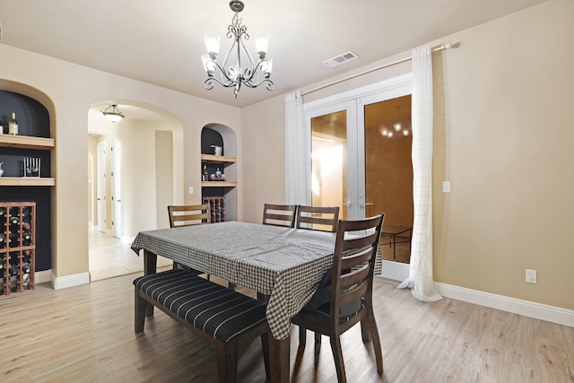 dining room with light hardwood / wood-style floors, built in features, french doors, and a notable chandelier