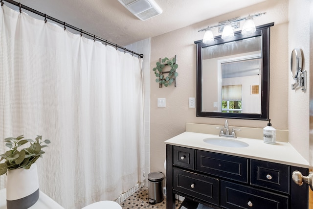 bathroom with a textured ceiling, toilet, vanity, and curtained shower