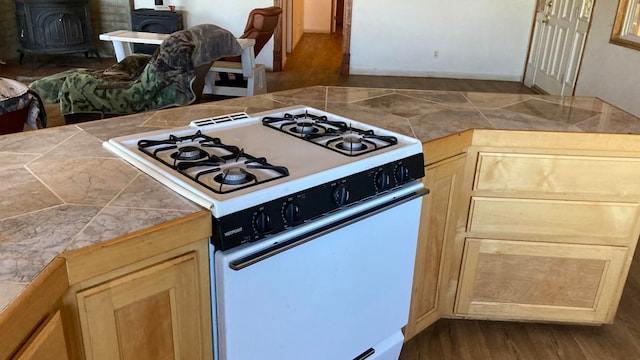 kitchen featuring light brown cabinets, wood-type flooring, tile counters, a wood stove, and white gas range oven