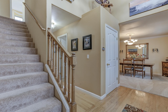 stairway featuring wood-type flooring, ornamental molding, and a chandelier