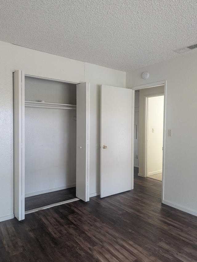 unfurnished bedroom featuring dark hardwood / wood-style flooring, a textured ceiling, and a closet