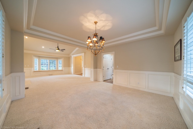 carpeted spare room featuring ceiling fan with notable chandelier, a raised ceiling, and ornamental molding