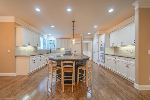 kitchen with an island with sink, light wood-type flooring, white cabinetry, and ornamental molding