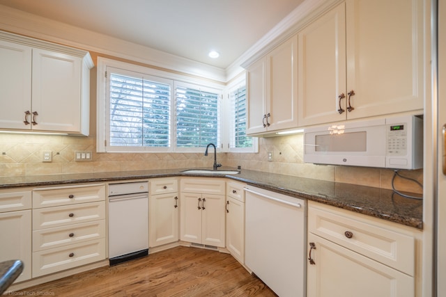 kitchen with light wood-type flooring, sink, backsplash, white appliances, and dark stone countertops