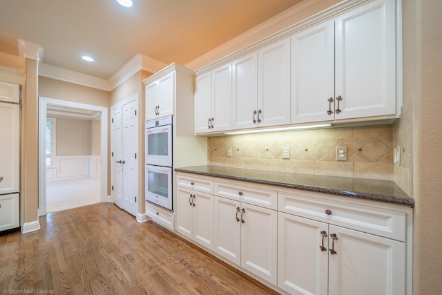 kitchen featuring ornamental molding, white cabinets, dark stone countertops, and light hardwood / wood-style floors