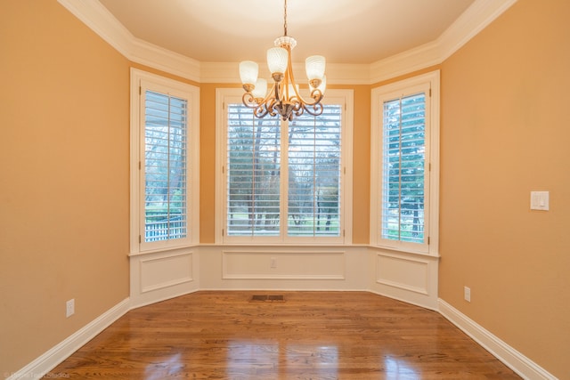 unfurnished dining area with hardwood / wood-style flooring, crown molding, and a notable chandelier