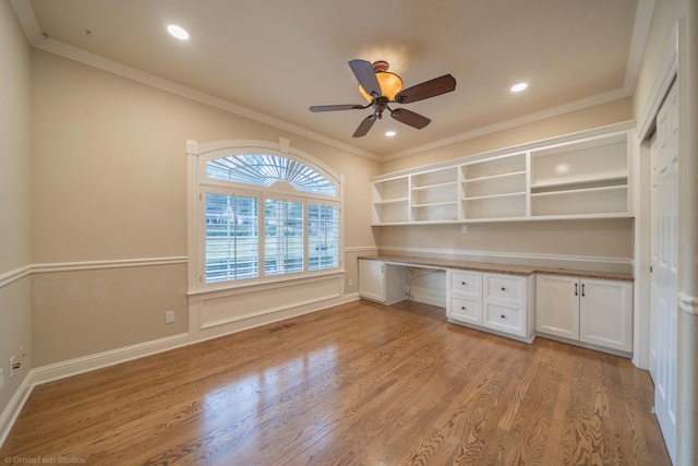 unfurnished office featuring light hardwood / wood-style flooring, built in desk, and crown molding