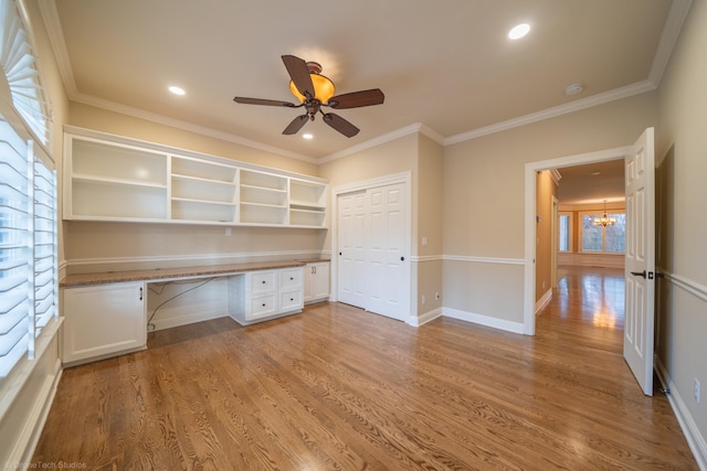 unfurnished office featuring hardwood / wood-style flooring, built in desk, and crown molding