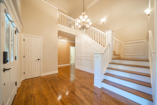 staircase with wood-type flooring, a notable chandelier, a towering ceiling, and ornamental molding