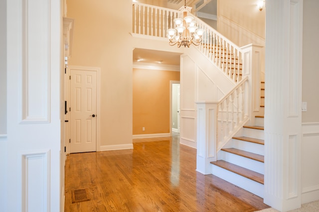 stairway featuring wood-type flooring, a towering ceiling, a chandelier, and crown molding