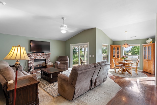 living room with ceiling fan, hardwood / wood-style flooring, a brick fireplace, and vaulted ceiling