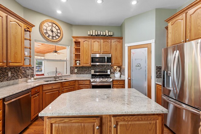 kitchen with tasteful backsplash, sink, light stone countertops, appliances with stainless steel finishes, and a center island